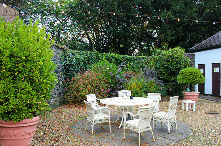 Tre-Ysgawen Hall woodland garden with sculptures and lush seasonal plants in a tranquil setting.